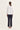 A woman shown from the back wearing a white three-quarter sleeve top and dark navy pants by Verge, standing against a plain off-white studio background.
