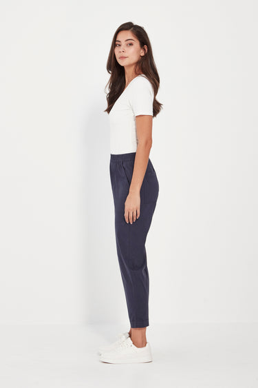 Woman wearing a white top and dark pants by Verge on a white background