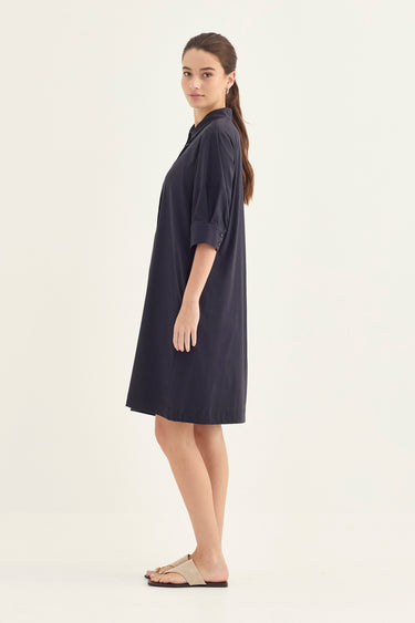 A woman modeling a dark navy blue shirt dress by Verge with three-quarter sleeves, shown in profile against a plain off-white studio background.