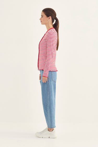 A woman shown in profile wearing a red and white horizontally striped long-sleeve top, light blue jeans by Verge, and white sneakers against a plain off-white studio background.