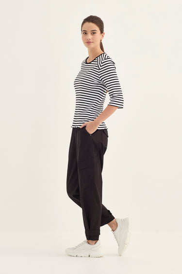 A woman modeling a black and white horizontally striped short-sleeve top, black jogger pants by Verge, and white sneakers agains a plain white studio background.