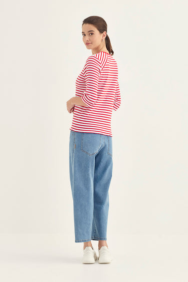 A woman modeling a red and white horizontally striped long-sleeve top, paired with light blue cropped jeans by Verge and white sneakers, photographed against a plain white studio background.