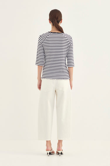 A woman shown from the back wearing a navy and white striped three-quarter sleeve top, white cropped trousers by Verge, and white heeled sandals against a plain off-white studio background.