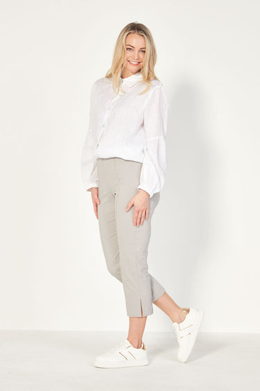 A woman modeling a white, button-through collared shirt by Verge with bracelet-length sleeves and a gathered feature just above the elbow. The shirt has an elasticated cuff, back yoke and back collar with ruched detail, and falls to the top of the thigh with side splits.