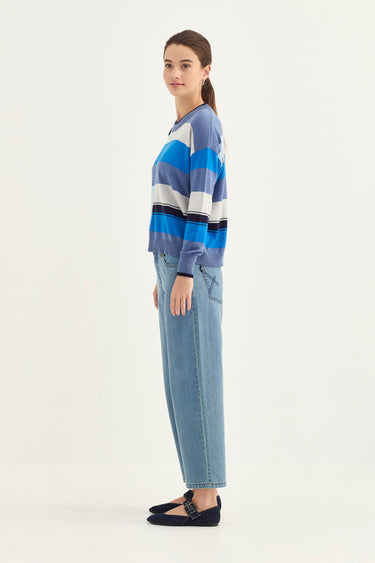 Woman wearing a blue and gray striped sweater and jeans by Verge on a white background
