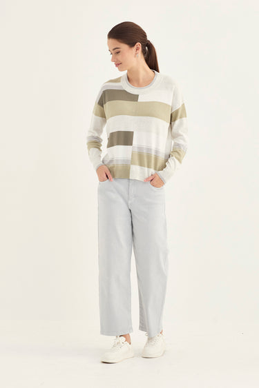Woman wearing a patterned sweater and light gray pants by Verge on a white background