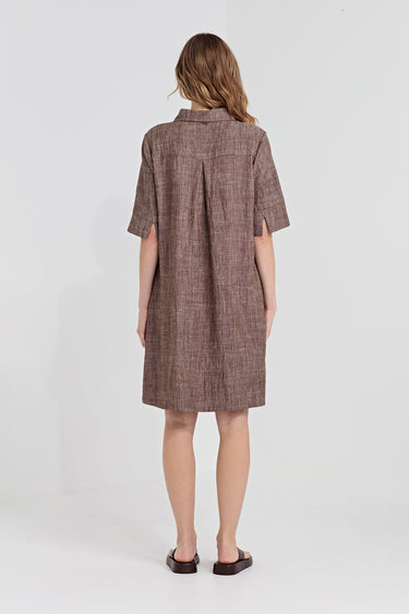 A woman viewed from the back wearing a short-sleeve plaid shirt dress by Verge in cocoa, paired with white heeled sandals, against a light gray studio background.
