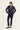 A woman modeling a dark navy blue quilted zip-up jacket with matching dark navy pants by Verge and flats, standing against a plain off-white studio background.
