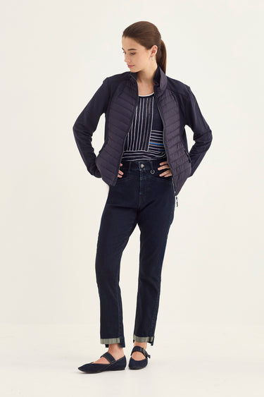 A woman modeling a dark navy blue quilted zip-up jacket with matching dark navy pants by Verge and flats, standing against a plain off-white studio background.