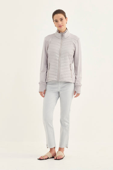 A woman modeling a light gray zip-up puffer jacket with a mock neck, paired with matching light gray pants and flat sandals by Verge, against a plain off-white studio background.