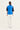 A model shown from the back wearing a bright blue quilted puffer vest over a black short-sleeve top and white wide-leg trousers by Verge, against a plain white studio background.