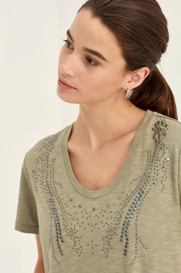 A woman wearing a short-sleeve olive green t-shirt by Verge with silver rhinestone embellishments on the chest, shown in a close-up profile shot against a plain white background.