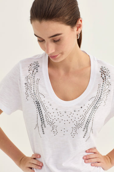 A woman wearing a white scoop-neck t-shirt by Verge with silver rhinestone embellishments on the chest, photographed against a plain light background.