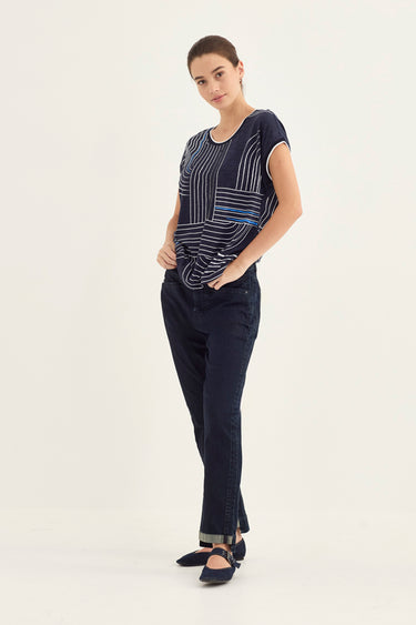 A woman modeling a navy blue short-sleeve top with white vertical stripes and dark navy pants by Verge, standing against a plain off-white studio background.