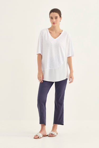 A woman modeling a white short-sleeve V-neck top and navy blue cropped pants by Verge against a plain white studio background.