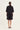 A model viewed from the back wearing a black short-sleeve cropped jacket and matching black shorts by Verge against a plain off-white studio background.