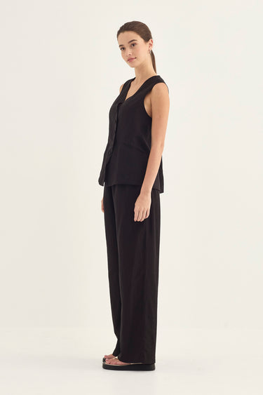 A woman modeling a black sleeveless vest and matching wide-leg trousers by Verge against a plain light background.