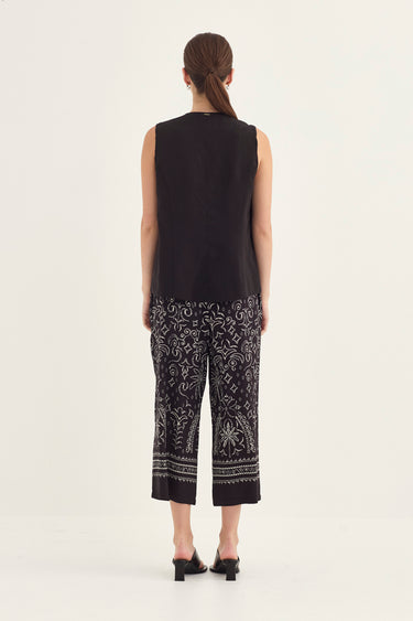 A model shown from the back wearing a sleeveless black top and black cropped pants by Verge with a white paisley bandana print, paired with black heeled sandals, against a plain off-white studio background.