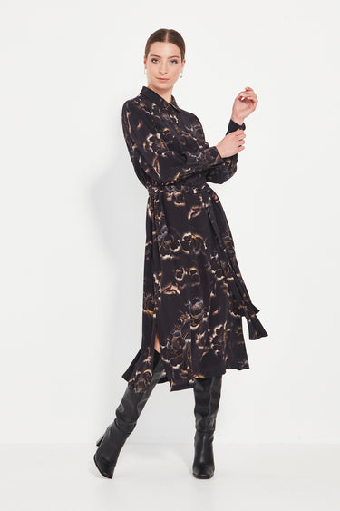 Woman wearing a black patterned dress from Verge with black boots on a white background.