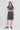 A woman modeling a short-sleeved, knee-length dark gray textured dress with a split neckline by Verge, paired with black slide sandals, against a plain light gray studio background.