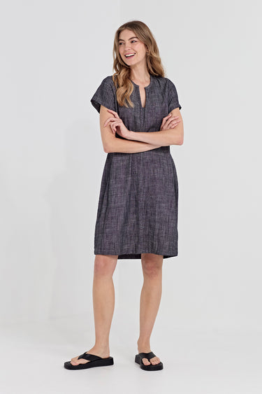 A woman modeling a short-sleeved, knee-length dark gray textured dress with a split neckline by Verge, paired with black slide sandals, against a plain light gray studio background.