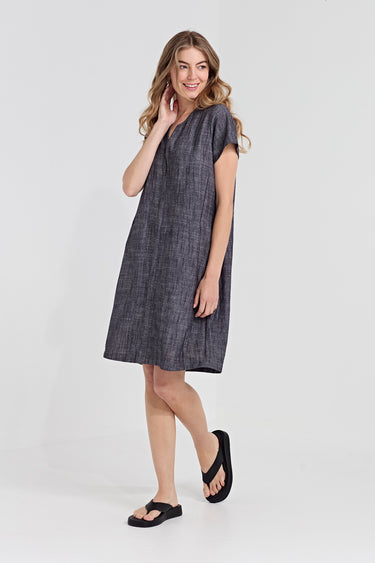 A woman modeling a short-sleeve, knee-length gray linen dress by Verge with a textured weave, paired with black flip-flop sandals, against a plain light gray studio background.