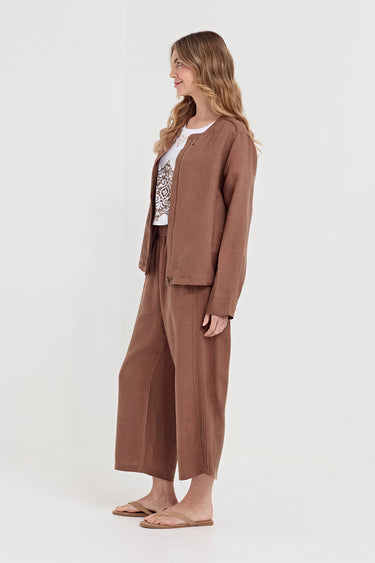 A woman modeling a matching brown two-piece lounge set consisting of a cropped button-front jacket and wide-leg cropped pants by Verge, styled over a white graphic tee and tan sandals against a plain white studio background.