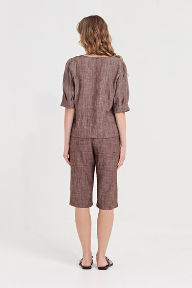 A woman viewed from the back wearing a matching brown textured linen-like two-piece set consisting of a short-sleeve top and knee-length shorts by Verge, paired with black flat sandals, against a plain white studio background.