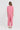 A woman viewed from the back wearing a matching pink two-piece outfit consisting of a short-sleeve cropped top and wide-leg cropped pants by Verge, paired with tan sandals, against a plain light gray studio background.