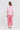 A woman viewed from the back wearing a pink and white striped short-sleeve t-shirt and pink cropped trousers by Verge, standing against a light gray studio background.