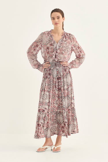 A woman modeling a long-sleeved midi dress with a dusty rose and gray abstract floral pattern by Verge, standing against a plain off-white studio background.