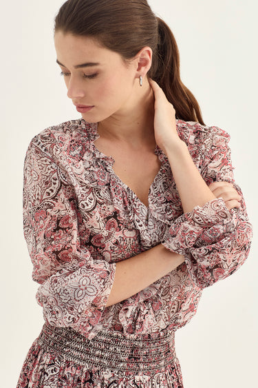 A woman wearing a long-sleeve V-neck dress with a dusty rose and black paisley pattern by Verge, photographed against a clean off-white background.