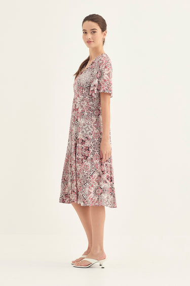 A woman modeling a short-sleeve midi dress with a pink, purple, and white floral pattern by Verge, standing against a plain light background.