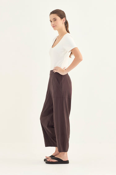 Woman wearing a white top and Chocolate Homeland Pants by Verge on a white background