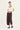 Woman wearing a white top and Chocolate Homeland Pants by Verge on a white background