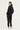A woman wearing a matching black tracksuit, consisting of a long-sleeve zip-up jacket and jogger pants by Verge, shown from a rear three-quarter view against a plain white studio background.