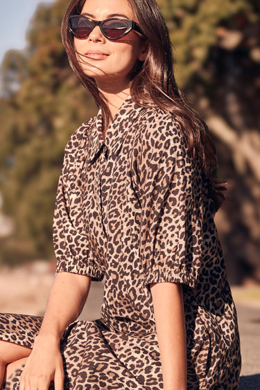 Woman wearing a leopard print dress and sunglasses outdoors.