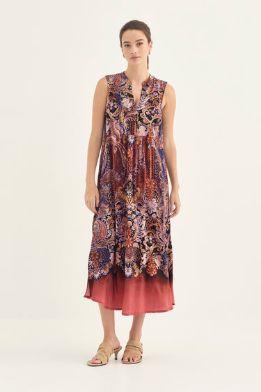 A woman modeling a sleeveless midi dress with a complex multicolor paisley and floral print dress by Verge, set against a plain off-white studio background.