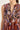 Close-up of a sleeveless V-neck dress by Verge with a busy paisley and floral print in purple, blue, red, gold, and cream tones, shown on a model against a plain light background.