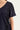 Close-up of a person wearing a dark navy short-sleeve top by Verge with black lace applique panels along the shoulder and side, against a plain light background.