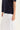 A close-up of a person wearing a dark navy short-sleeve top and a white skirt by Verge with a large front patch pocket, against a plain light background.