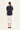 A woman viewed from behind wearing a dark navy short-sleeve t-shirt and a white midi skirt by Verge, standing against a plain off-white studio background.