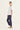 A woman modeling a white short-sleeve V-neck top and navy blue cropped pants by Verge, standing in a side profile against a plain off-white studio background.