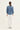 A woman viewed from the back wearing a dusty blue long-sleeve top with puffed shoulders and white wide-leg jeans by Verge, standing against a plain white studio background.