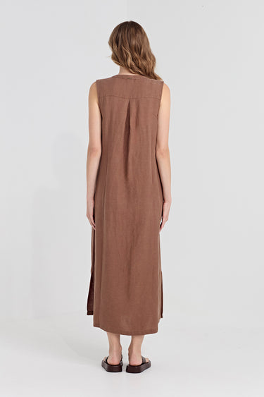 A woman viewed from the back wearing a sleeveless brown maxi dress by Verge with side slits and a gathered neckline, standing against a plain light gray studio background.