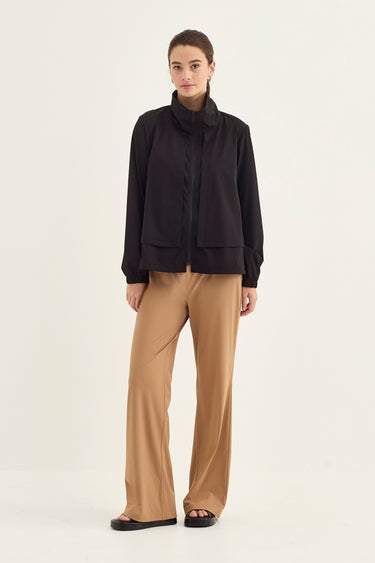 A model stands against a plain light background wearing a tan cropped zip-front jacket with long sleeves and a high collar, paired with wide-leg tan pants by Verge, against a plain light background.