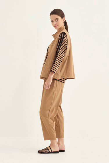 A woman modeling a tan two-piece outfit consisting of a sleeveless zip-front jacket with black-and-tan striped sleeves and matching cropped pants by Verge, photographed against a plain light background.