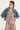 A woman wearing a light blue denim jacket over a sleeveless V-neck dress with a pink, beige, and black paisley pattern by Verge, posed against a plain off-white studio background.