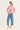 A woman modeling a light pink long-sleeve knit cardigan with a scalloped hem, paired with light blue cropped jeans by Verge and white slide sandals, against a plain off-white studio background.