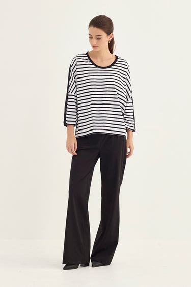 A woman modeling a black and white horizontally striped long-sleeve top with black trim, paired with black wide-leg pants by Verge, against a plain light gray studio background.